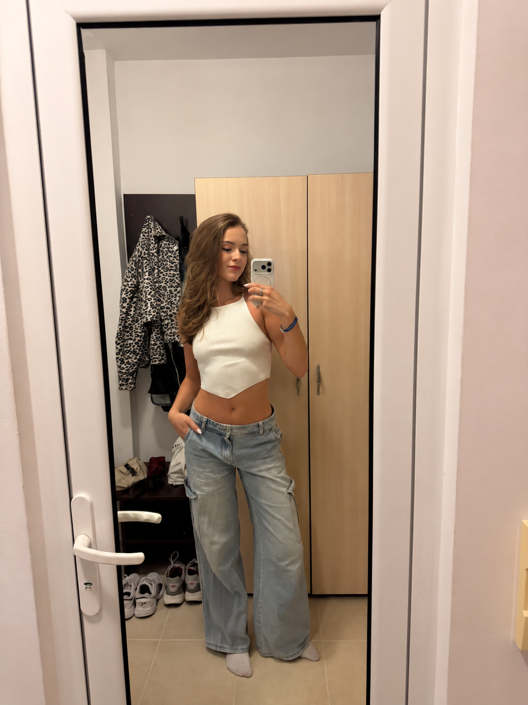 Lucy in a cream top and jeans, taking a mirror photo