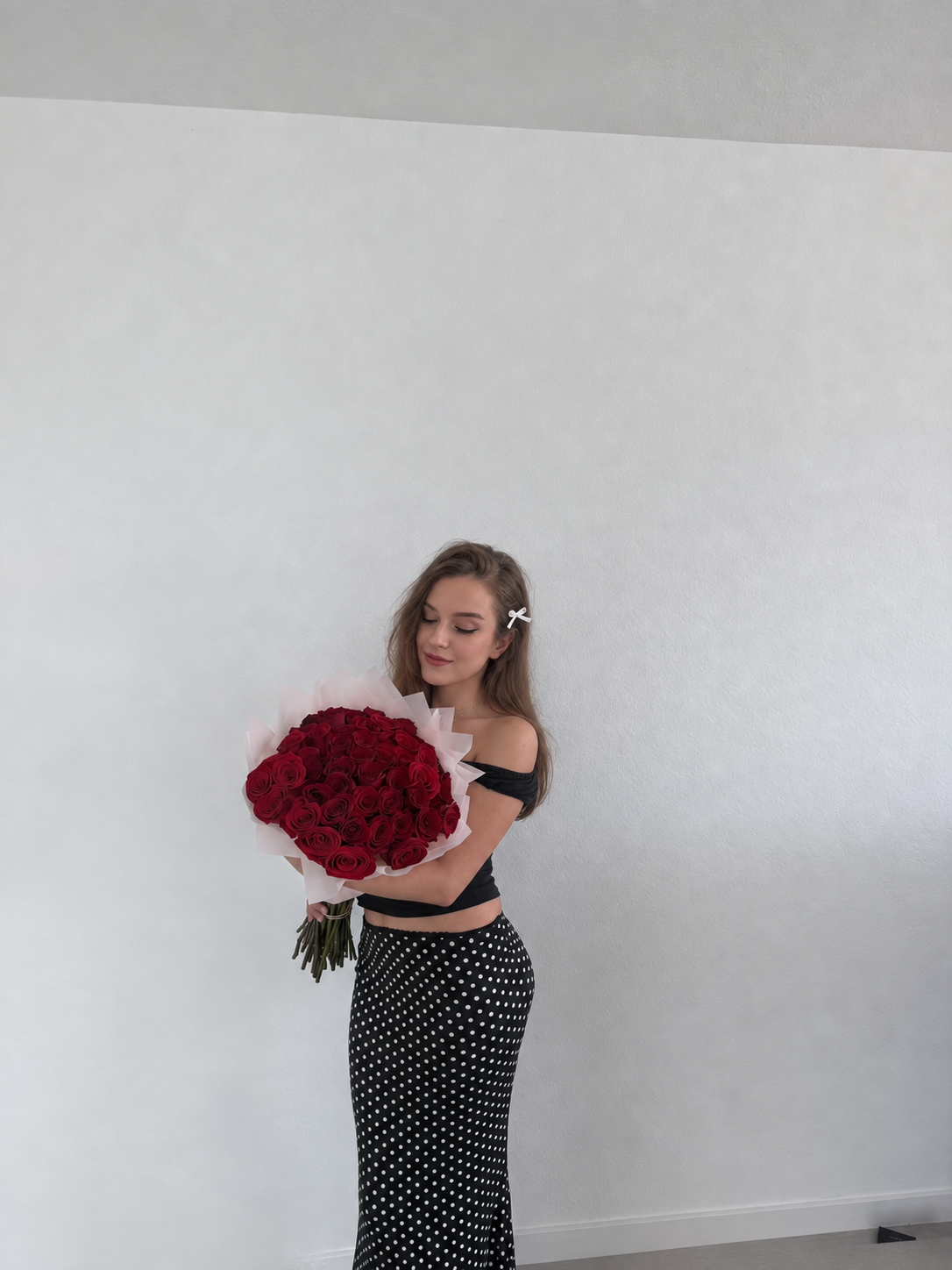 Lucy holding a bouquet of red roses, wearing a black top and spotted skirt