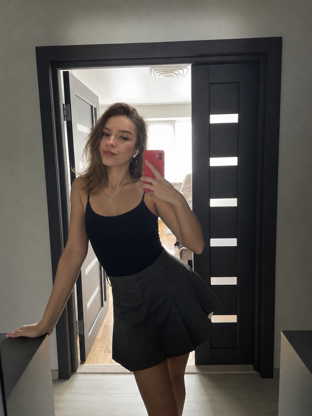Lucy in a black top and grey skort, taking a mirror photo